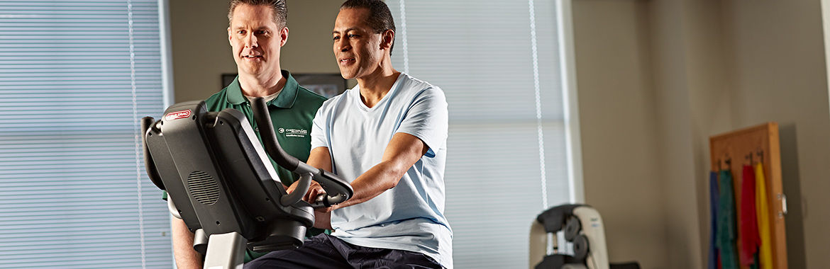 A man works with a therapist on a stationary bicycle