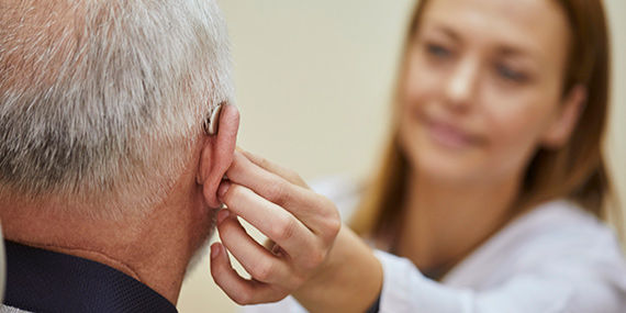 An audiologist fits an older man with a hearing aid.