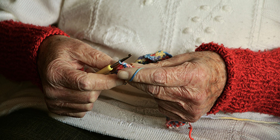 Una mujer mayor tejiendo a crochet, enfocada en sus manos
