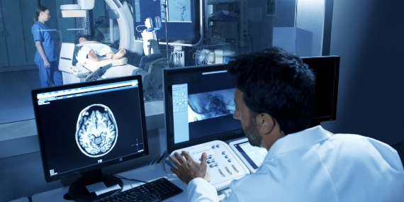 Un médico que observa un estudio de exploración mientras el paciente está en la sala de pruebas