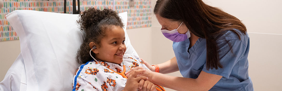 Una niña escucha su propio corazón a través de un estetoscopio mientras recibe atención de un médico