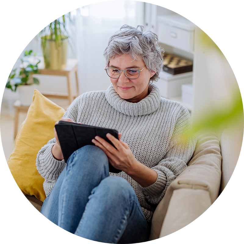 Mature woman using digital tablet while sitting on sofa at home