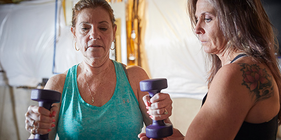 A woman works with hand weights with a physical therapist