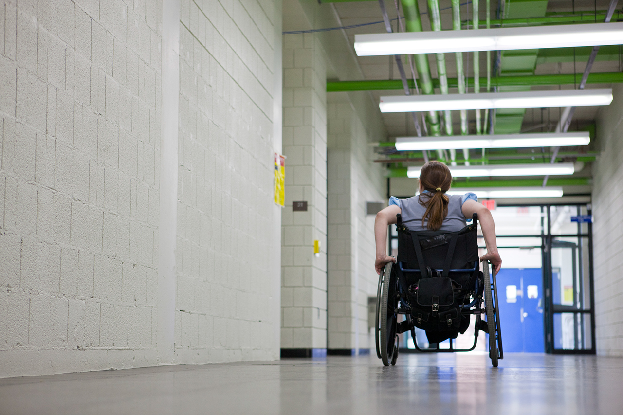 Woman with Spina Bifida in corridor of college in wheelchair.