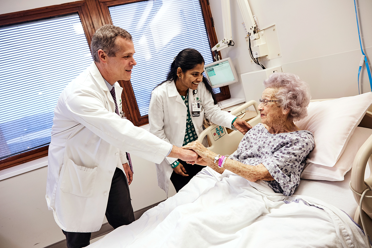Doctors talk with an elderly patient in a hospital bed.