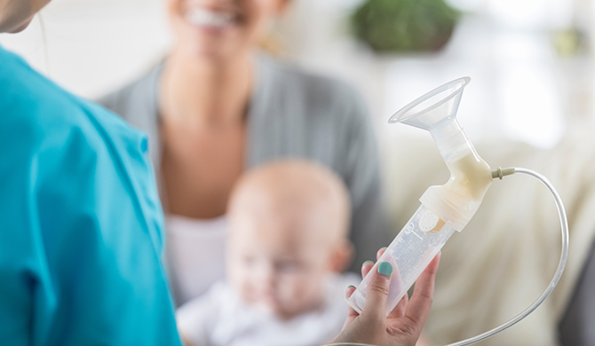 Enfermera sosteniendo un dispositivo de ayuda para la lactancia junto a una madre y un niño