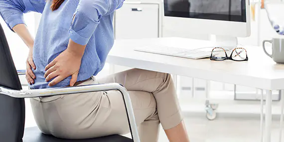 Woman sitting at computer holding her back