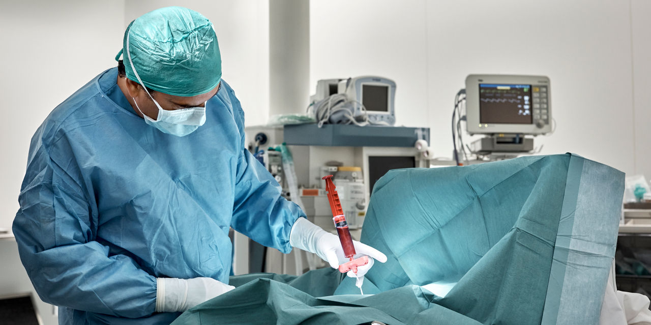 Mature suregon monitoring bone marrow extraction procedure donw on patient in operating room at hospital