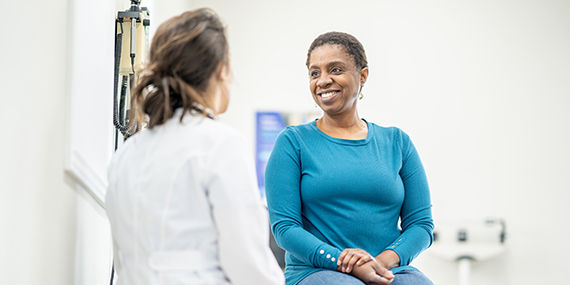 A Black woman sits on an examining table while speaking to a medical provider