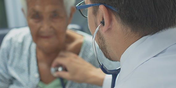 A doctor uses a stethoscope to listen to the heart of a senior man