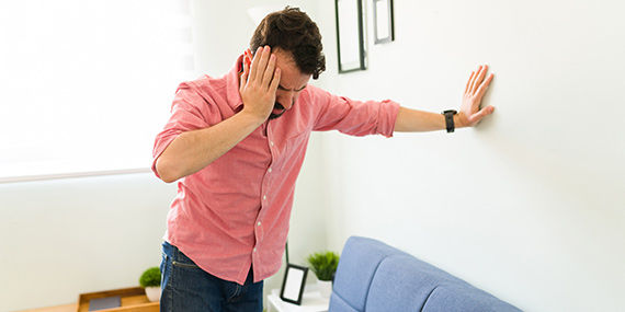 A man leans against the wall holding his head in discomfort.