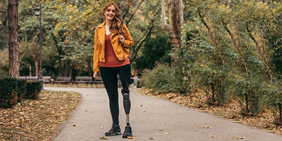 A young woman with a prosthetic leg stands on a path in a park