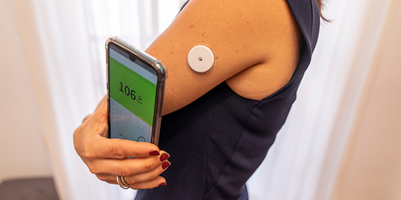 A diabetic uses their smartphone to read the constant glucose meter attached to their arm.