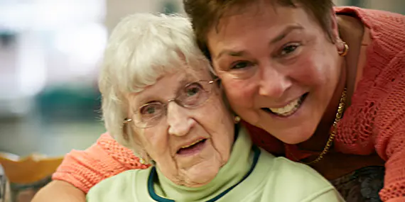 A caregiver hugs an elderly woman.