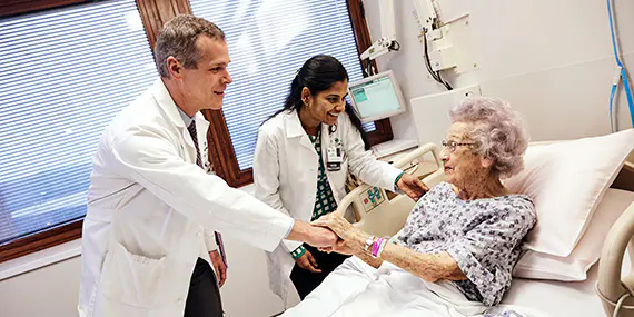 Doctors talk with an elderly patient in a hospital bed.