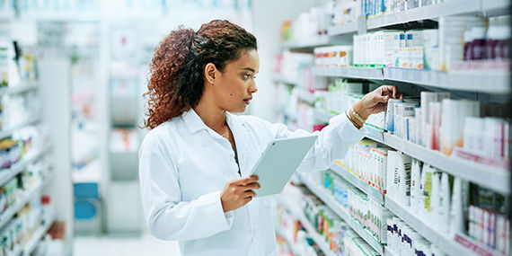 A young woman works in a pharmacy while using a digital tablet