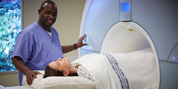A lab tech assists a patient as she is placed inside an MRI machine