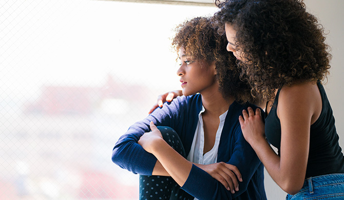 Woman looking out window being consoled