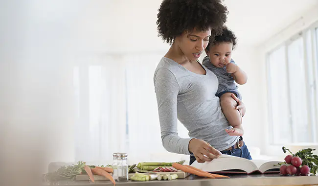 Mother holding her child while looking through a cook book