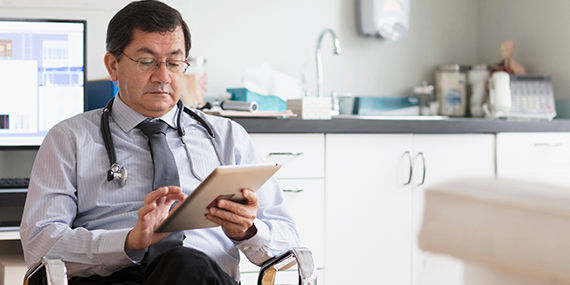 Male hispanic doctor sitting while using an electronic tablet