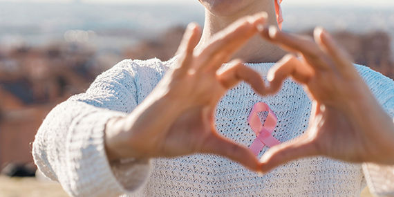 Woman making a heart shaped with her hands while using a pink ribbon for support breast cancer cause.