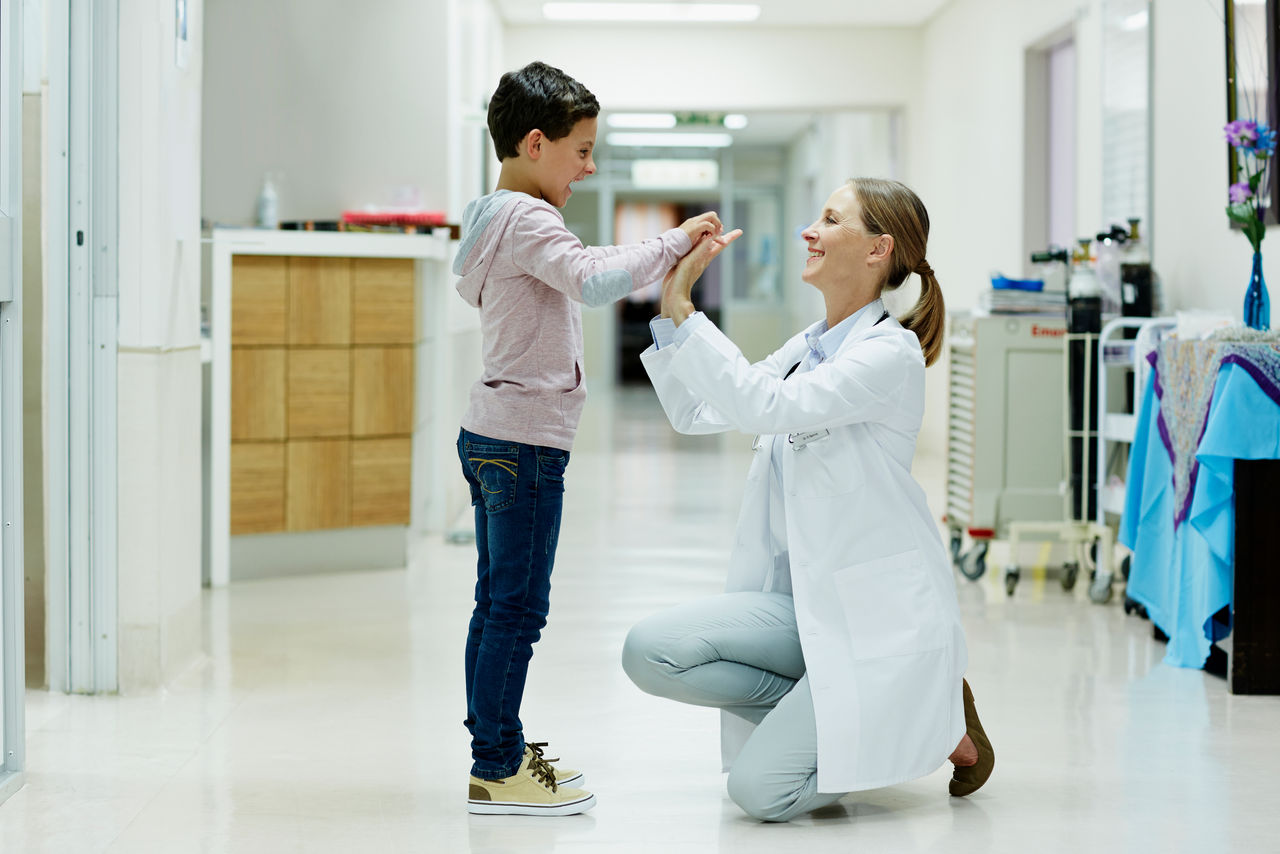 A female doctor kneels in front of a smiling child patient, giving each other a high five