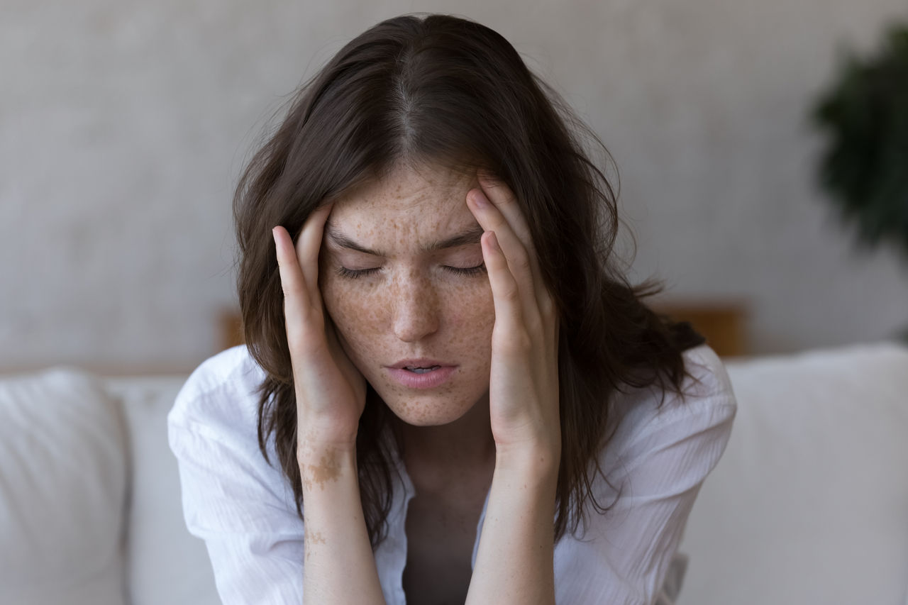 A young woman holds her head with her eyes closed while suffering a migraine.