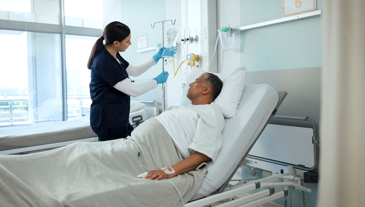 A man lies in a hospital bed while a female nurse checks his IV