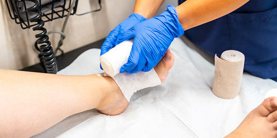 A medical professional wearing blue gloves wraps a bandage around a patient's foot