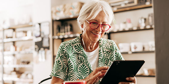 An older woman uses a tablet while sitting at a table with a cup of coffee