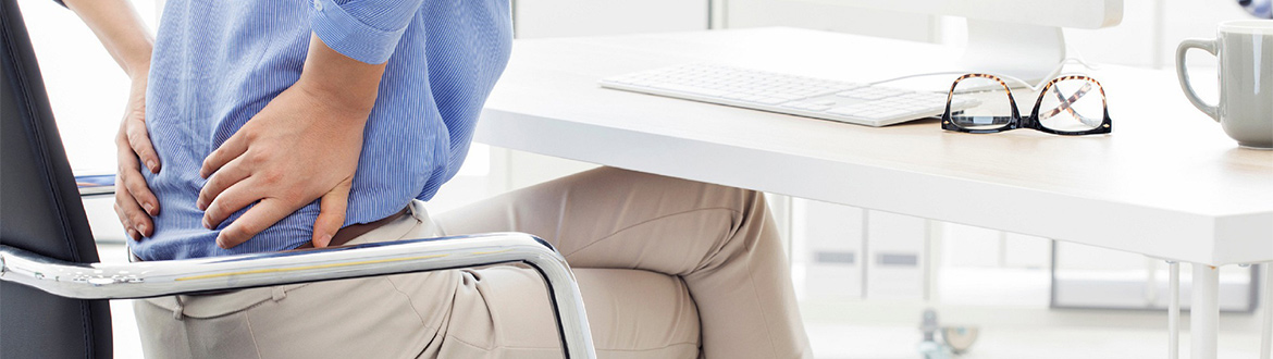 Mujer sentada usando una computadora y agarrándose la espalda