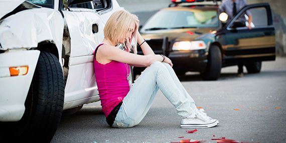 Una mujer que sufre dolor y está sentada junto a su automóvil después de un accidente