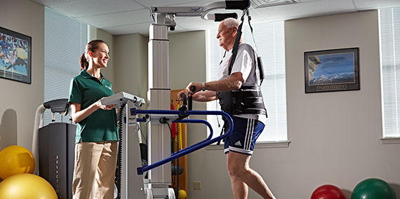 Un hombre mayor que recibe orientación en una terapia con sistema de arnés en una cinta caminadora