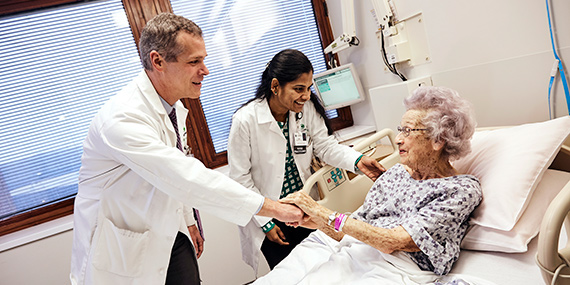 Los médicos hablan con un paciente de edad avanzada en una cama de hospital.