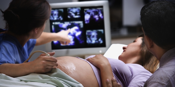 Una médica que señala la imagen de una ecografía junto a una embarazada