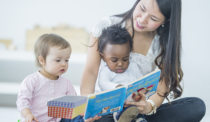 Young woman reading to two babies.