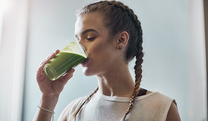 Young woman drinking vegetable smoothie in kitchen