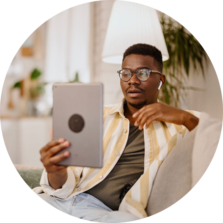 A Black man sites on a couch while reading from a tablet