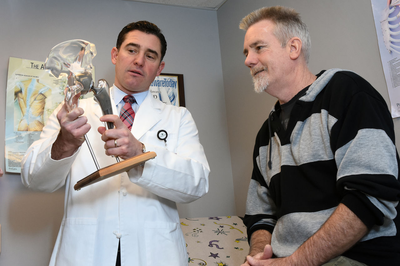 A patient looks on as a doctor shows an example of a hip replacement