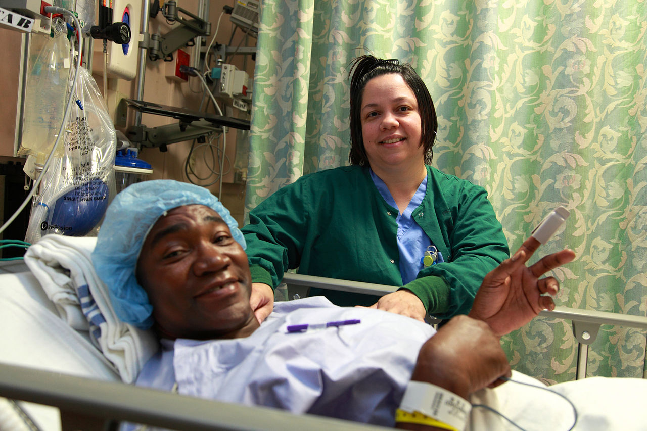 A man in a hospital bed receiving care from a nurse.