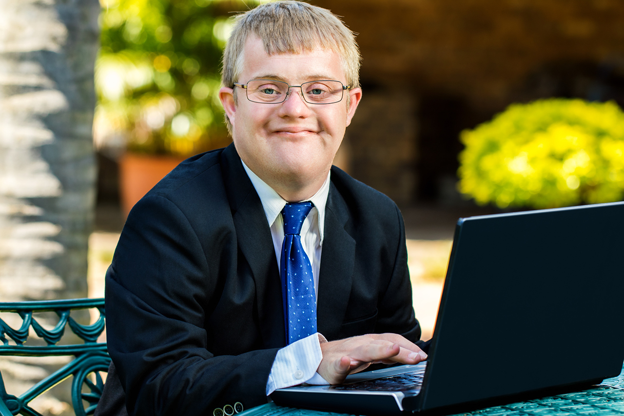 A young businessman with Down Syndrome working with a laptop.