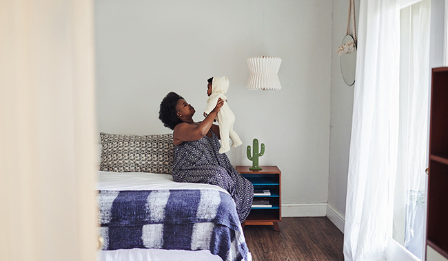 Motherat home on her bed, lifting her baby above her