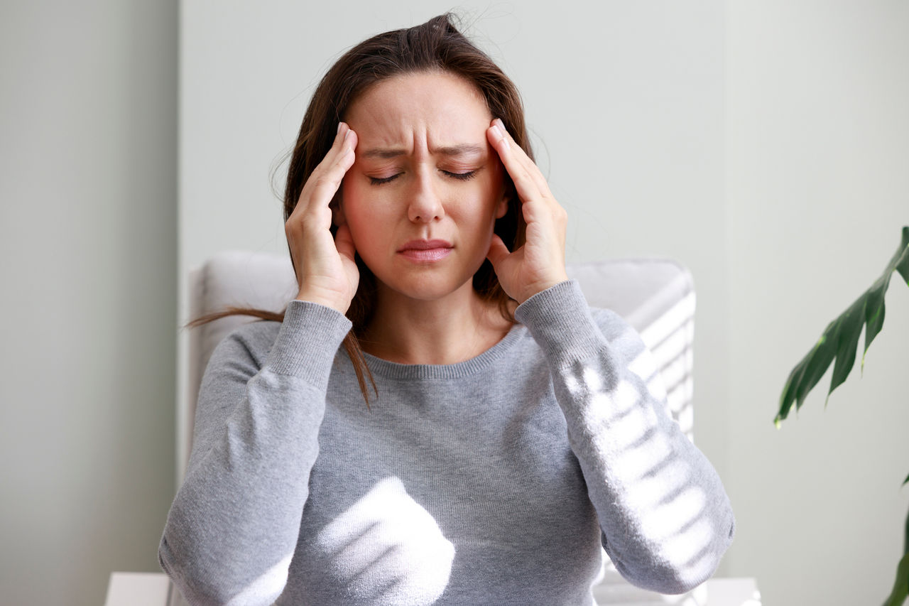 A young woman holds her head in pain due to migraine