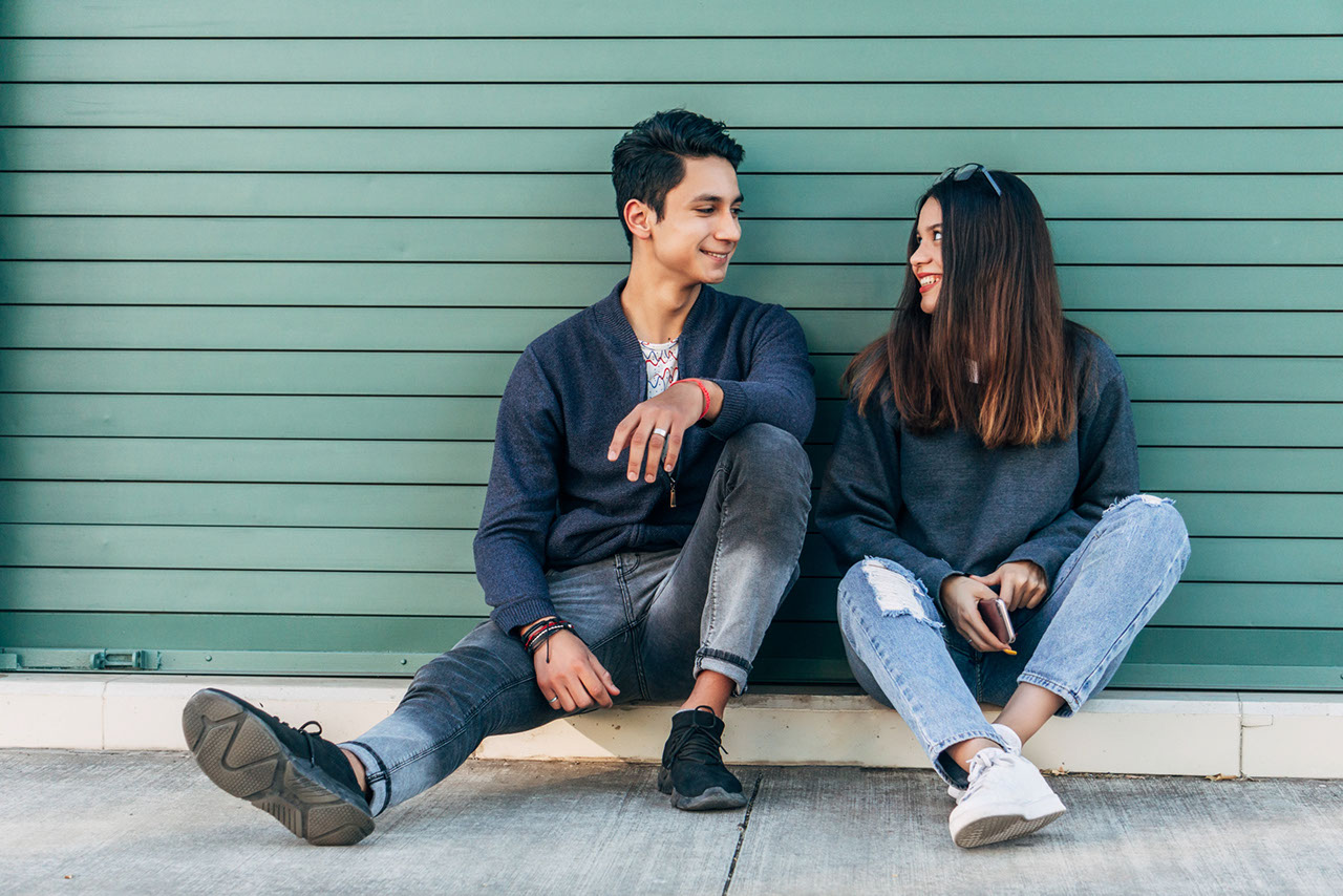 A teenage couple sitting on the sidewalk.