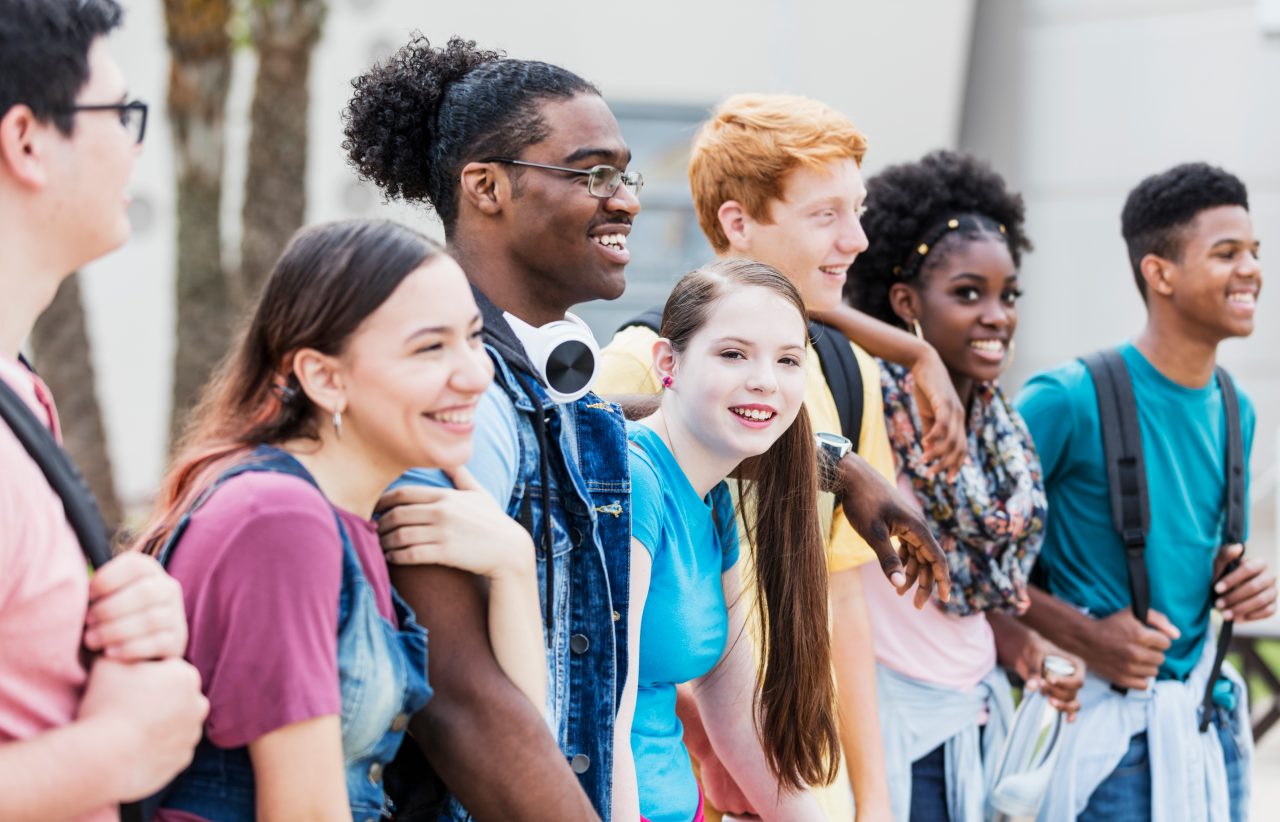 A diverse group of teenagers stands in a line smiling