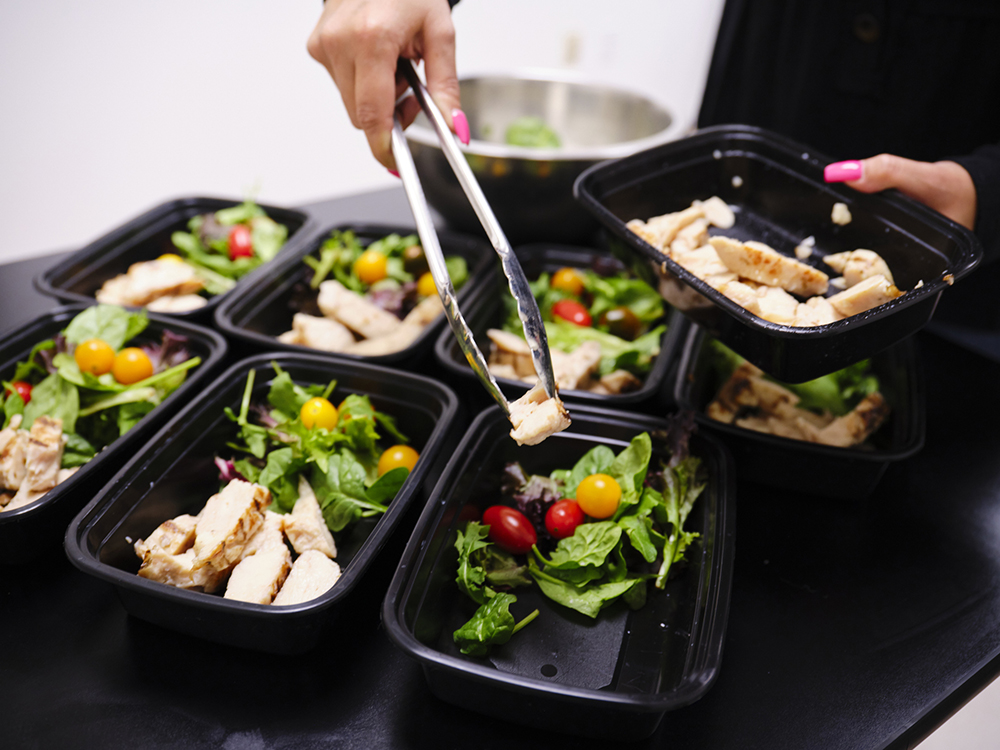 A woman prepares a healthy meal in her kitchen, using a scale to portion the ingredients.