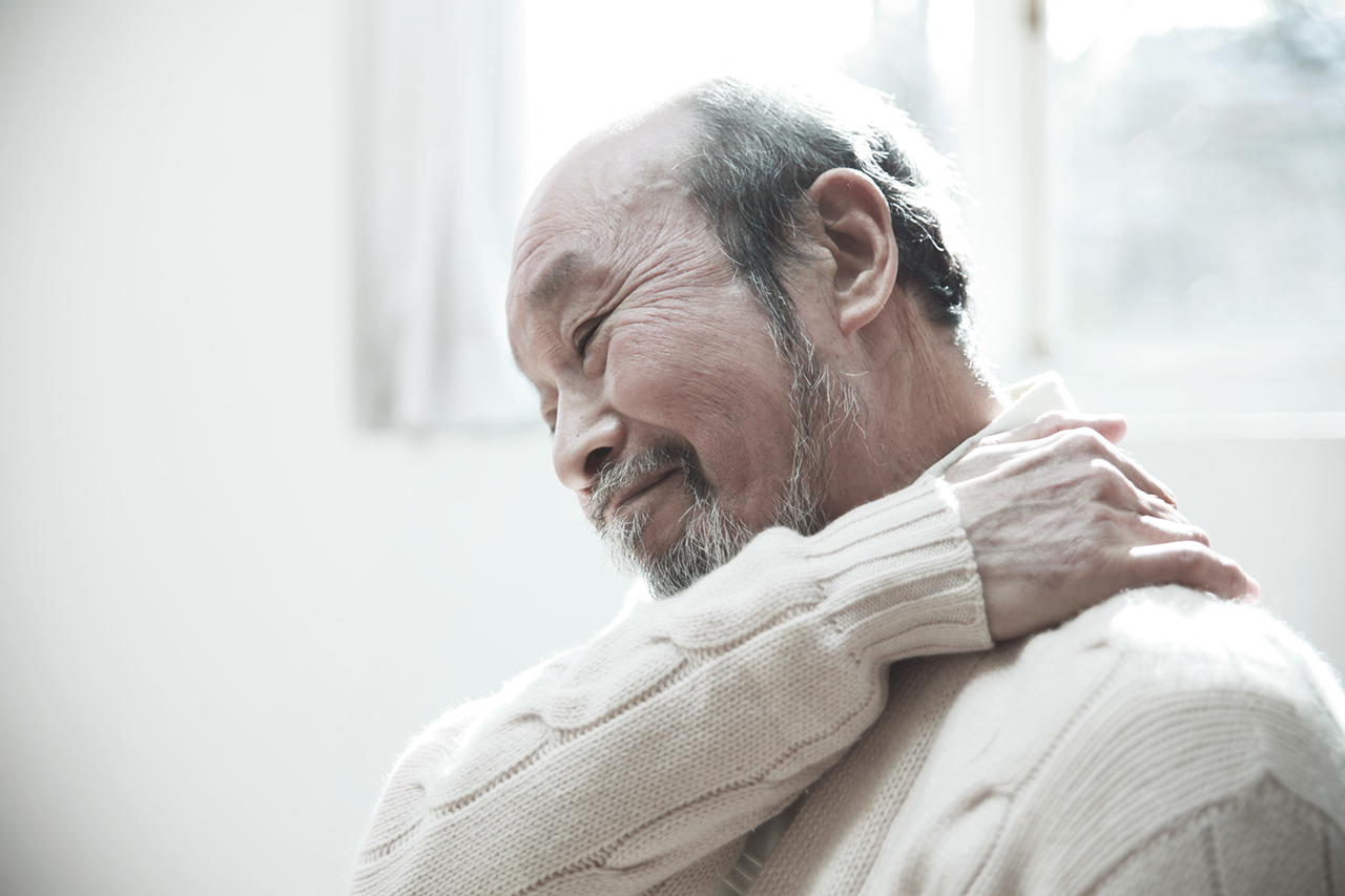 Un hombre mayor que se frota el cuello y el hombro para aliviar el dolor.